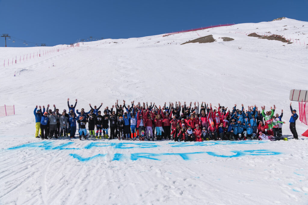 Photo de groupe prise à Tignes lors des championnats du monde de para ski alpin adapté. De nombreux athlètes et encadrants en tenues colorées posent bras levés sur la neige. Devant eux est écrit en grandes lettres bleues dans la neige « Alpes 2030 Virtus ». "Group photo taken in Tignes during the World Championships of adapted para alpine skiing. Many athletes and staff in colorful outfits pose with raised arms on the snow. In front of them, the words 'Alpes 2030 Virtus' are written in large blue letters in the snow